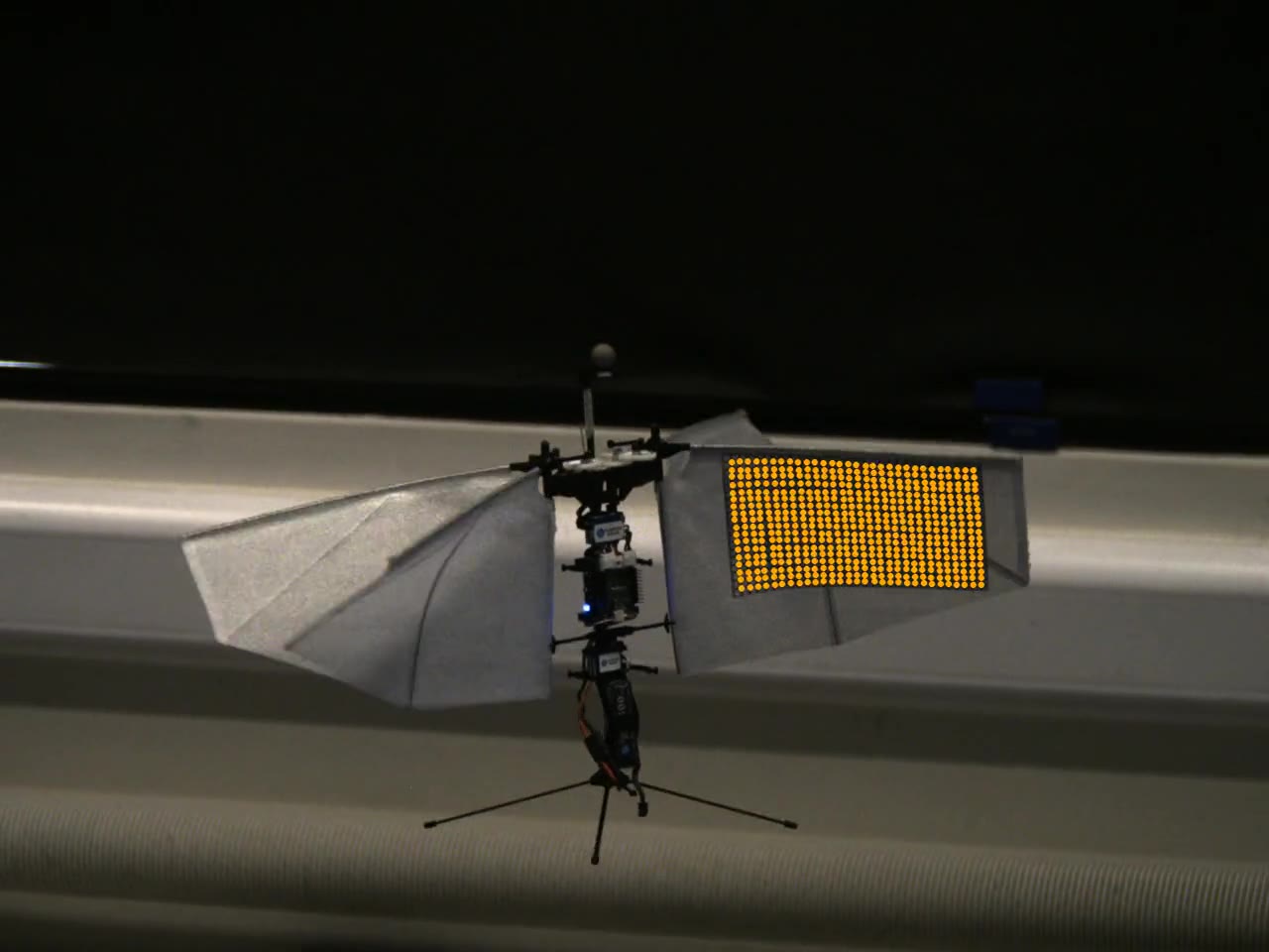 A flapping-wing drone in flight with a tracked dot-grid overlaid on its wing.